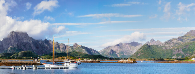 A picturesque view of a sailboat docked in a scenic fjord in Lofoten, surrounded by rugged mountains and clear blue skies. A perfect setting for an adventure and tranquil getaway. Lofoten, Norway
