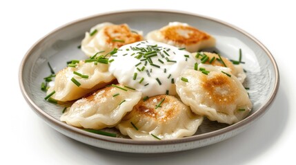 A plate of Polish pierogi with sour cream and chives on a white background.
