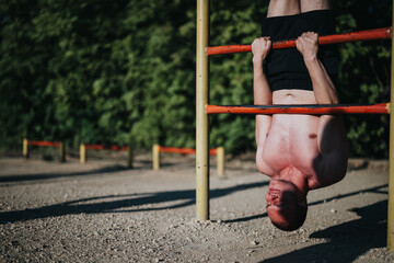 Fit man performs an inverted pull-up on a bar in an outdoor fitness park, showcasing strength and...