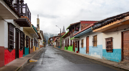 Street in Jardin, Jardín, Antioquia, Colombia. Green background, colorful colonial facades and houses. Clouds, church in the background.