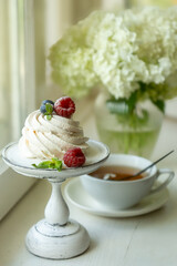 Tea in a beautiful white cup, cake with berries and white hydrangea flowers.