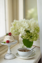 Tea in a beautiful white cup, cake with berries and white hydrangea flowers.