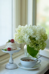 Tea in a beautiful white cup, cake with berries and white hydrangea flowers.