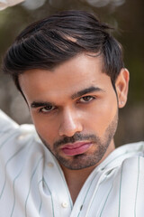 Close-up portrait of a confident, handsome Asian Indian man with his face directed towards the camera, showcasing his rich facial expressions, exuding a calm and peaceful demeanor.