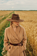 Obraz premium Stylish caucasian Blonde Woman in Brown Vintage Coat and hat on Wheat Field