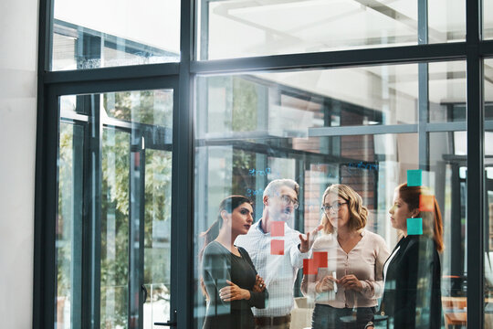 Woman, team and collaboration with notes on board with review, listening and planning with brainstorming. Coach, training and group by glass wall, questions and discussion with strategy in office