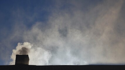 Silhouette of smoke against the sun from the chimney of a village house.