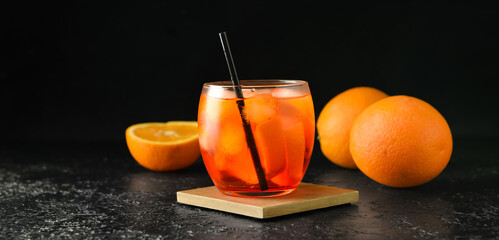 Glass of tasty aperol spritz cocktail and fresh oranges on dark background