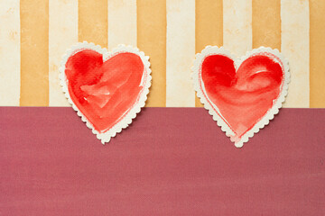 two paper hearts set against striped scrapbooking paper sheet and a solid ground