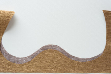 part of a gold crepe paper shape with curves and waves on blank paper