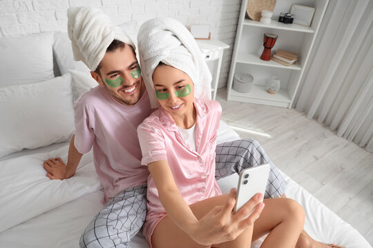 Young loving couple with under-eye patches taking selfie in bedroom - Powered by Adobe