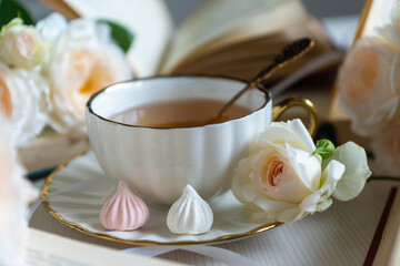 A cup of aromatic tea, a book and a rose on the table. May June July August.