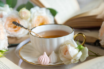 A cup of aromatic tea, a book and a rose on the table. May June July August.