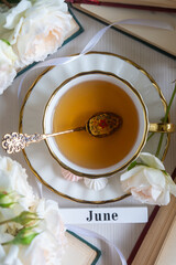 A cup of aromatic tea, a book and a rose on the table. May June July August.