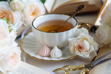 A cup of aromatic tea, a book and a rose on the table. May June July August.