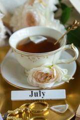 A cup of aromatic tea, a book and a rose on the table. May June July August.