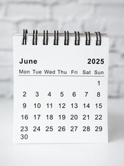 Minimalist, modern, and simple desk calendar for the year 2025 on a table with a white brick wall in the background. The cover of the calendar displays the text 2025 calendar