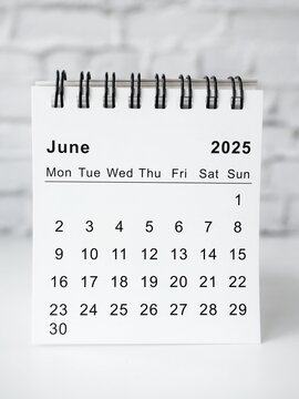 Minimalist, modern, and simple desk calendar for the year 2025 on a table with a white brick wall in the background. The cover of the calendar displays the text 2025 calendar