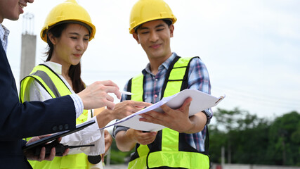 Fototapeta premium Close-up image of engineer and workers inspect plans outside, discussing project details and ensuring alignment
