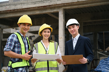 Smiling construction workers and an engineer or architect standing together at a construction site, holding plans and a clipboard, showcasing their collaborative effort in building a new project