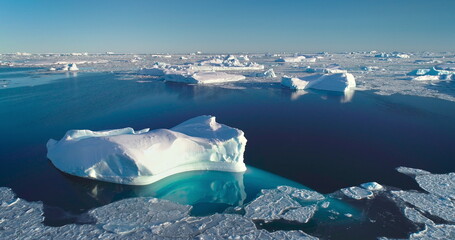 Tranquil Arctic scene icebergs floating blue ocean. Broken sea ice under bright blue sky sunlight. Glacier melting in polar summer, aerial. Ecology, melting ice, climate change, global warming concept