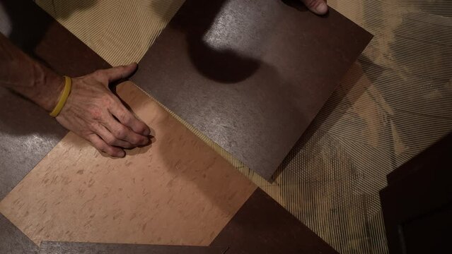 Closeup of hands putting a vinyl composition tile, VCT into place on a kitchen floor in a home renovation project.
