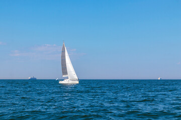 Obraz premium White sloop rigged yacht sailing in the Baltic sea at sunset. Clear sky after the storm, soft sunlight. Transportation, travel, cruise, sport, recreation, leisure activity, racing, regatta