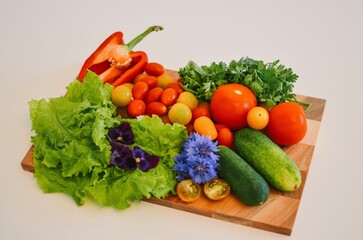 wooden board with vegetables like tomatoes, cucumbers, paprika and herbs on a white background