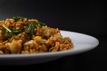 Close up side view photo of Homemade fried rice with vegetables, chicken and fried eggs served on a white plate with spoon and fork. Isolated on black background.