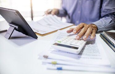 Fototapeta premium Asian businessman using a calculator to calculate expenses, taxes, financial documents and analyzing business data to plan for future business growth