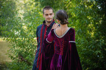 Man and woman in 19th century costumes in the forest. The couple is talking, the woman is standing with her back turned. Date