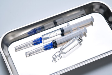 Syringes with needles and an ampoule in a stainless steel medical tray.