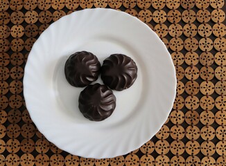 Three round chocolate-covered marshmallows are clustered together on a white plate.
