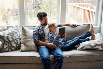 Father, child and tablet on sofa with internet for educational gaming, movie bonding and online tv show. Family, man and boy with digital tech on couch in living room for relax, streaming and happy