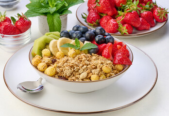 Granola with strawberries, kiwi, banana and blueberries in a round plate on a white table. Healthy and tasty food