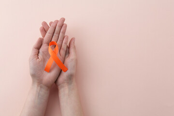 Woman with orange awareness ribbon on beige background, top view. Space for text