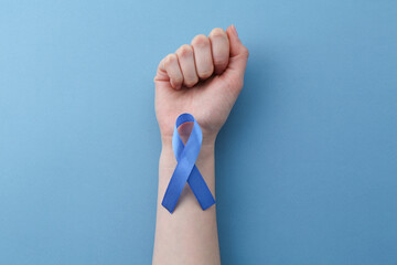 Woman with blue awareness ribbon on color background, top view