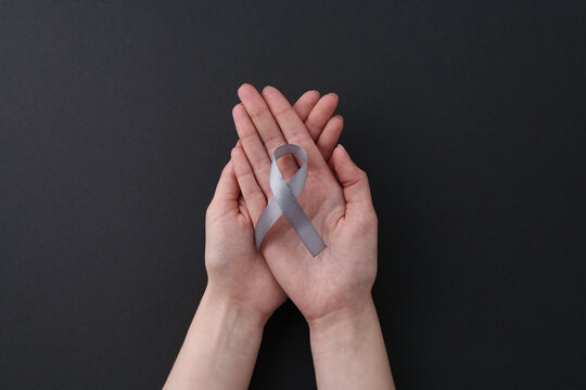 Woman with grey awareness ribbon on black background, top view