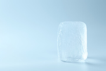 Block of clear ice on light blue background, space for text