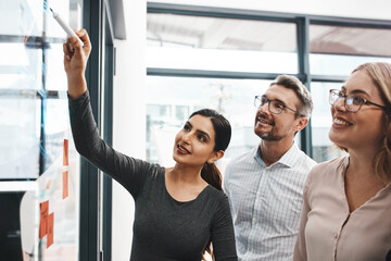 Woman, teamwork and office with writing on glass board with notes, discussion and planning with brainstorming. Coach, training and group by wall, synergy and collaboration with strategy in workplace