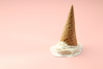 Melted ice cream in wafer cone on light pink background. Space for text
