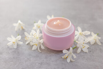 Cream in jar and beautiful jasmine flowers on grey table, closeup