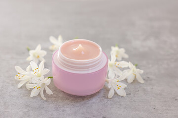 Cream in jar and beautiful jasmine flowers on grey table, closeup