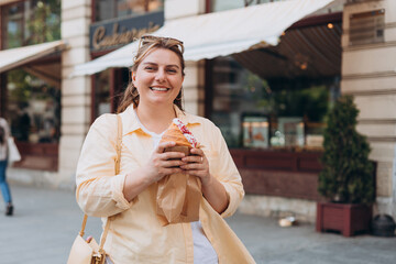 Beautiful overweight brunette 30s girl posing on the street, she has big croissant meal in hands....