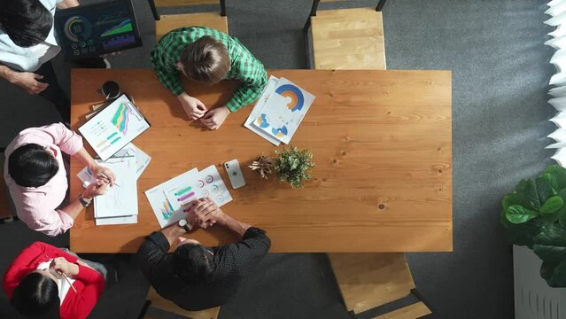 Top view of business man using tablet display increasing graph while diverse marketing people sharing idea or planing strategy at meeting table with stock market statistic scatter around. Convocation.