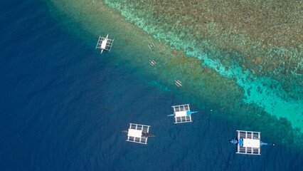 Breathtaking aerial view of Balicasag Island, Philippines showcasing local bankas amidst vibrant coral reefs teeming with marine life.