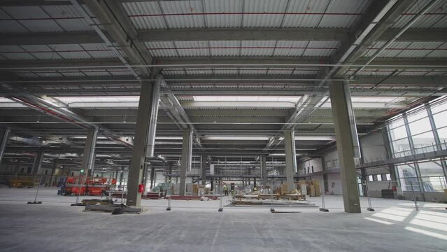Interior of large production hall under construction. Modern newly built industrial building. Prefabricated columns and beams supporting steel roof.