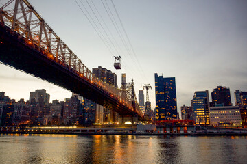 The Queensboro Bridge at Golden Hour while the Roosevelt Island Tram heads across on its cables over the East River with the Manhattan skyline in the background