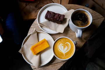 Coffee break. Two mugs of American and latte art on a wooden background. Chocolate brownie and yuzu cake slices. Delicious sweet food and coffees. Flat white, latte. Food and drink.
