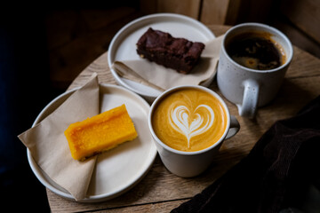 Coffee break. Two mugs of American and latte art on a wooden background. Chocolate brownie and yuzu cake slices. Delicious sweet food and coffees. Flat white, latte. Food and drink.